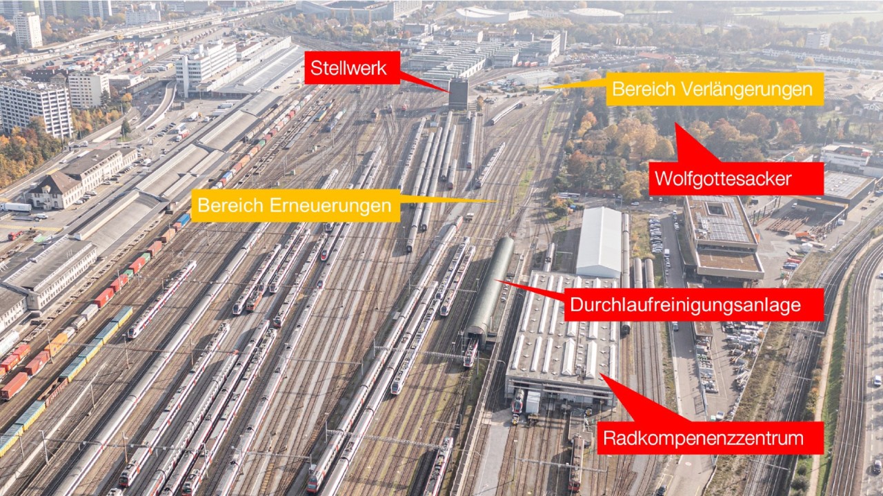 Das Foto vom Oktober 2021 zeigt die Abstellanlagen von Westen (Bahnhof Basel SBB) in Richtung Osten (Muttenz) gesehen. Oben, in der Mitte des Bildes ist das turmartige Stellwerk zu sehen. Rechts davon liegt der Bereich, bis zu welchem die Abstellgleise verlängert werden. Rechts von diesem liegt der Wolfgottesacker. Vor dem Stellwerk, zwischen den Hauptgleisen Richtung Muttenz und dem Wolfgottesacker, liegt die heutige Abstellanlage, welche erneuert wird. Im unteren Bildbereich, rechts von der Abstellanlage, sind die Durchlaufreinigungsanlage und das Radkompetenzzentrum zu sehen. 