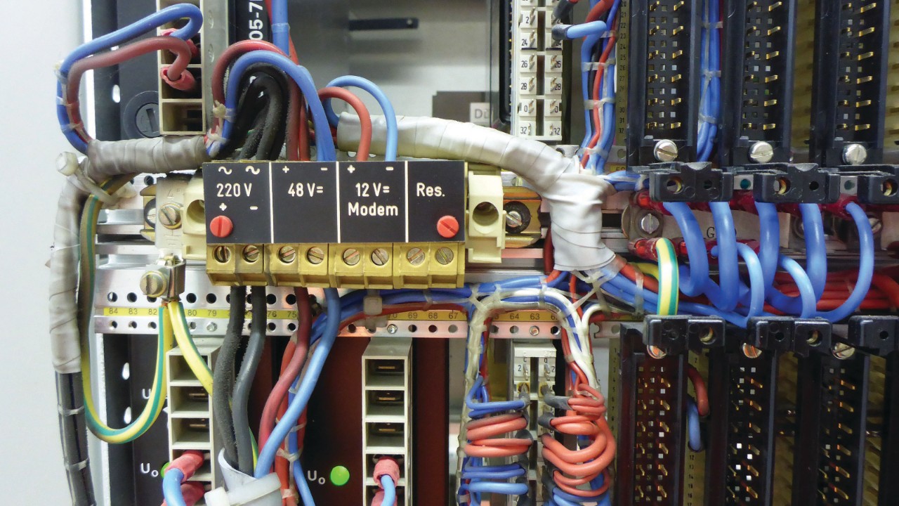 Une photo montre une partie du câblage d’une alimentation sans interruption. Différents câbles de couleur sont pourvus d’étiquettes spécifiques de tension et d’appareils.