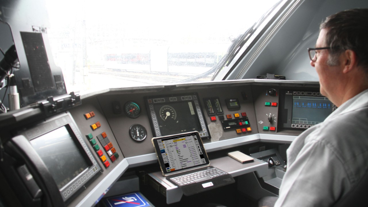 Ein Lokführer sitzt im Führerstand eines ICN-Zugs und betrachtet sein Tablet mit der angezeigten Pünktlichkeitsanzeige.  