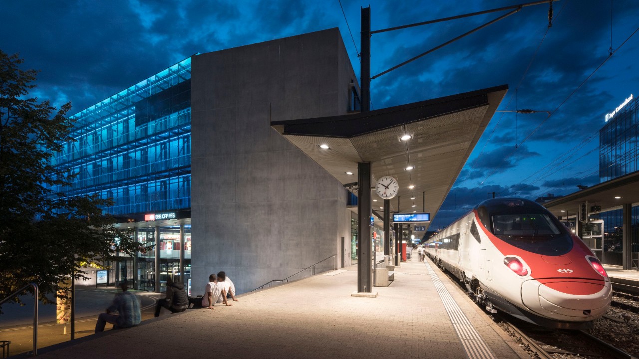 Das Bild zeigt einen wartenden Zug an einem beleuchteten Perron an einem Bahnhof.