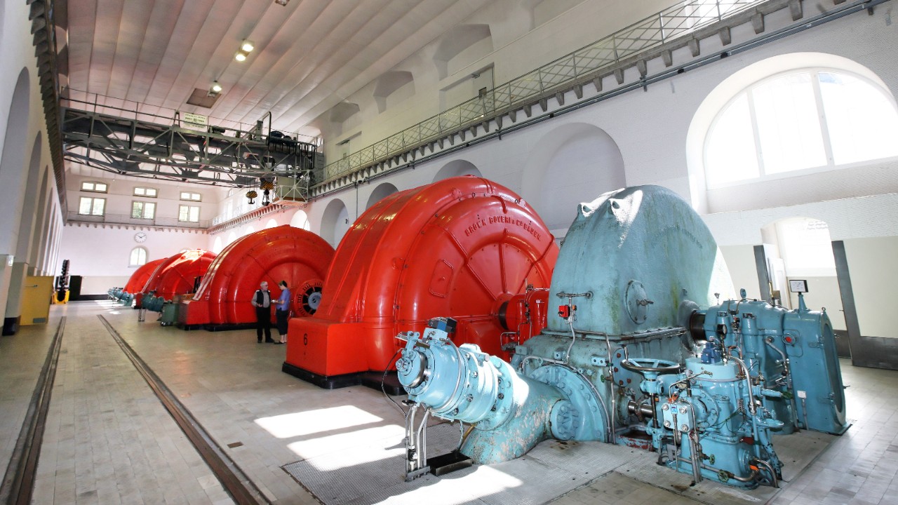 Abgebildet sind die Turbinen und Generatoren in einem Wasserkraftwerk. Die Steuerung der Wassermenge erfolgt mit den Peltondüsen.
