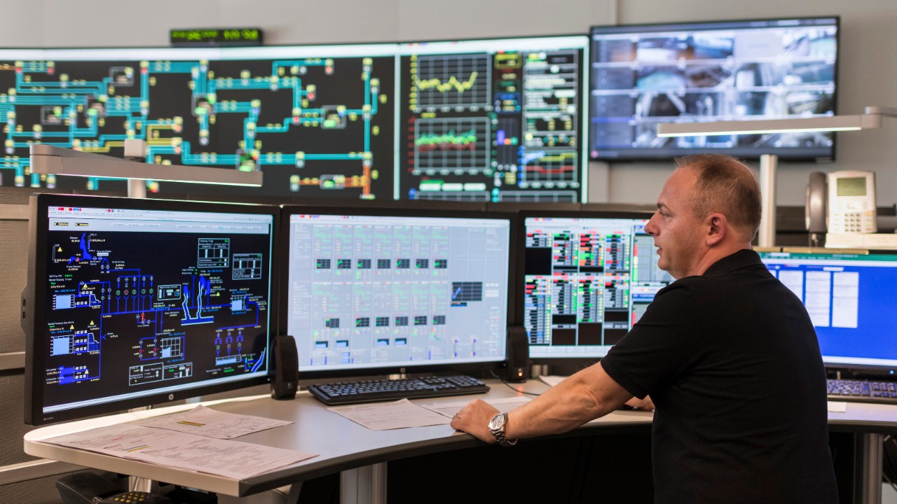 Das Foto zeigt in einem Raum mehrere Bildschirme mit der Darstellung vom Bahnstromnetz, im Vordergrund kontrolliert eine Person die aktuelle Situation.