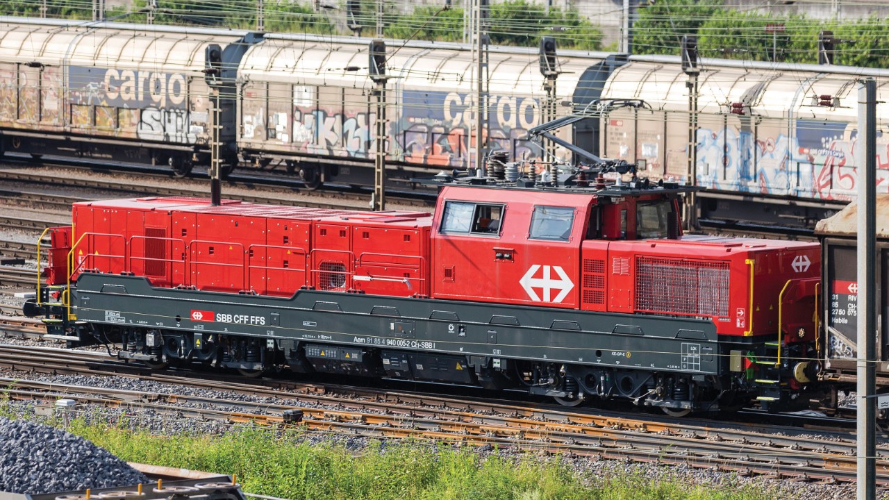 Locomotiva per il traino di treni merci rossa Aem 940 ferma sui binari di una stazione ferroviaria.