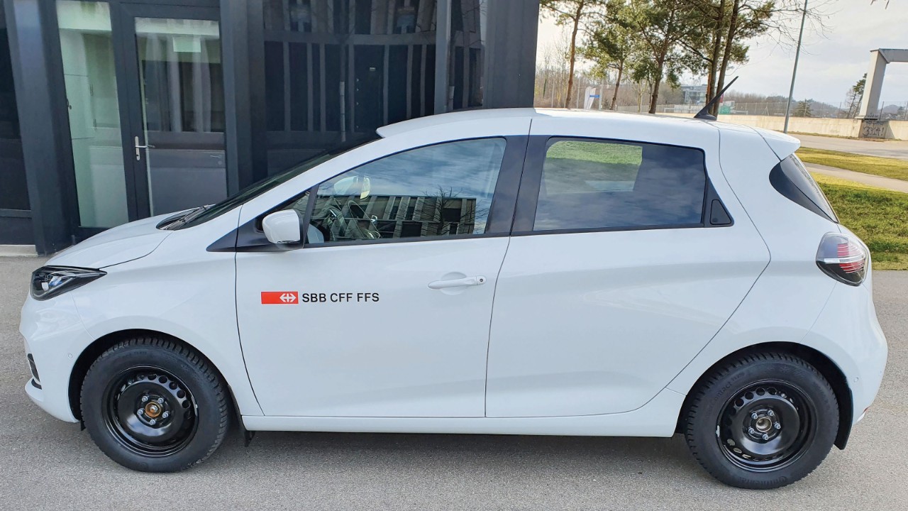 L’immagine mostra un’auto elettrica bianca con il logo delle FFS, parcheggiata davanti a un edificio adibito a uffici.