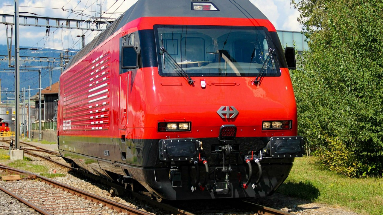 La foto mostra una locomotiva Re 460 rossa davanti a un’officina.