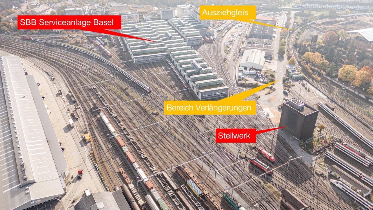 Das Foto vom Oktober 2021 zeigt die Abstellanlagen von Nordwesten (Seite Zeughaus) in Richtung Südosten (Dreispitz) gesehen. Oben, in der Bildmitte, liegt die imposante SBB Serviceanlage Basel. Rechts von ihr ist der Bereich zu sehen, bis zu welchem die Abstellgleise verlängert werden. Recht davon, zwischen dem besagten Bereich und dem Wolfgottesacker, verläuft in einer Schlaufe das Ausziehgleis, welches zurückgebaut wird. Rechts der Bildmitte, im unteren Bildbereich, sieht man das turmartige Stellwerk. 