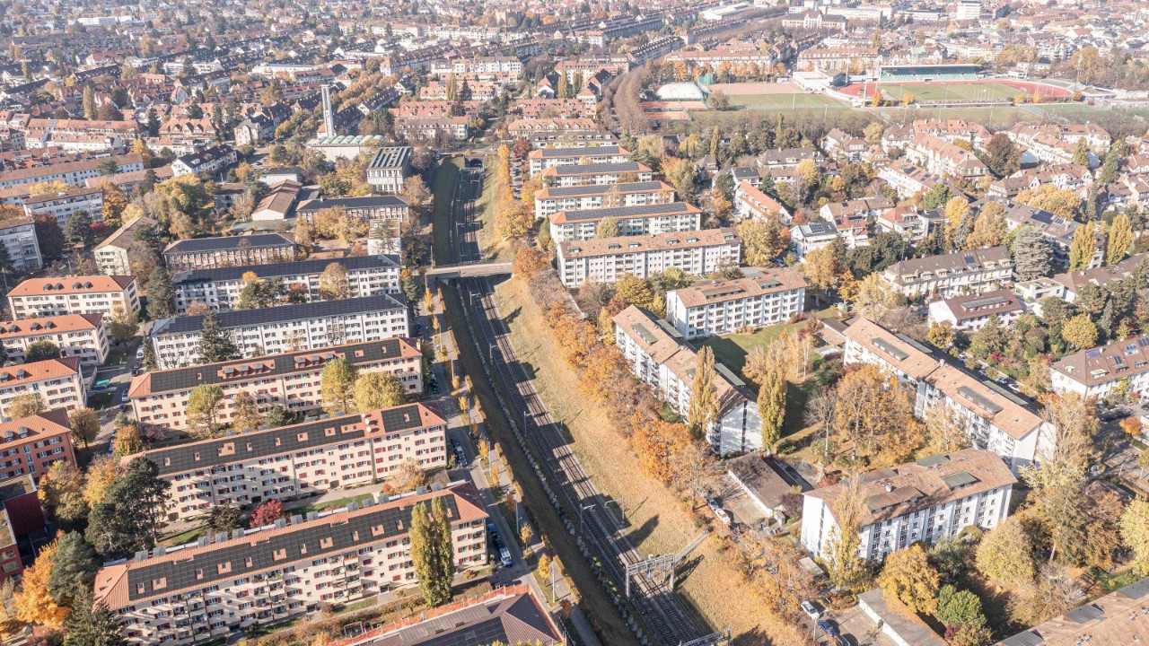 Das Luftbild zeigt die Zufahrt zum Südportal des Schützenmatttunnels in Basel. Umgeben von Wohngebäuden und herbstlich gefärbten Bäumen, verbindet es städtische und natürliche Elemente.