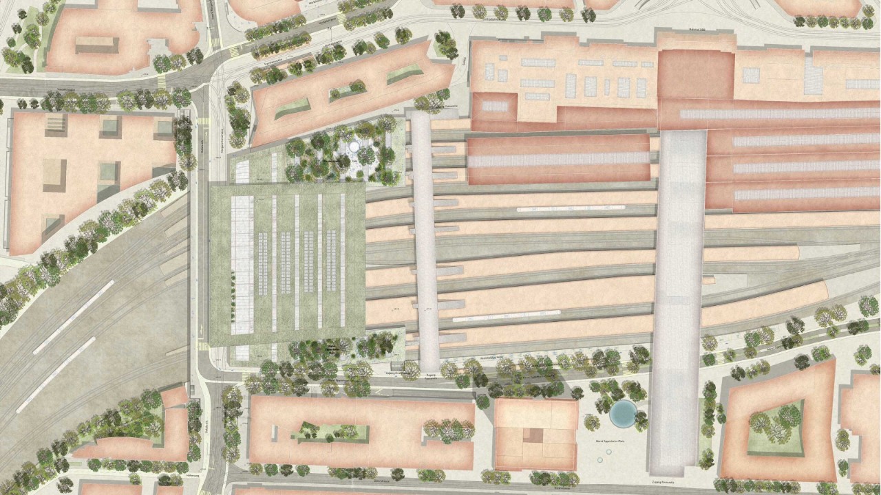 Das Bild zeigt eine detaillierte Luftaufnahme eines Bahnhofsbereichs mit mehreren Gleisen, Perrons und umliegenden Gebäuden. Es gibt Bäume und Grünflächen um den Bahnhof herum. Die Straßen und Wege sind ebenfalls deutlich zu erkennen.