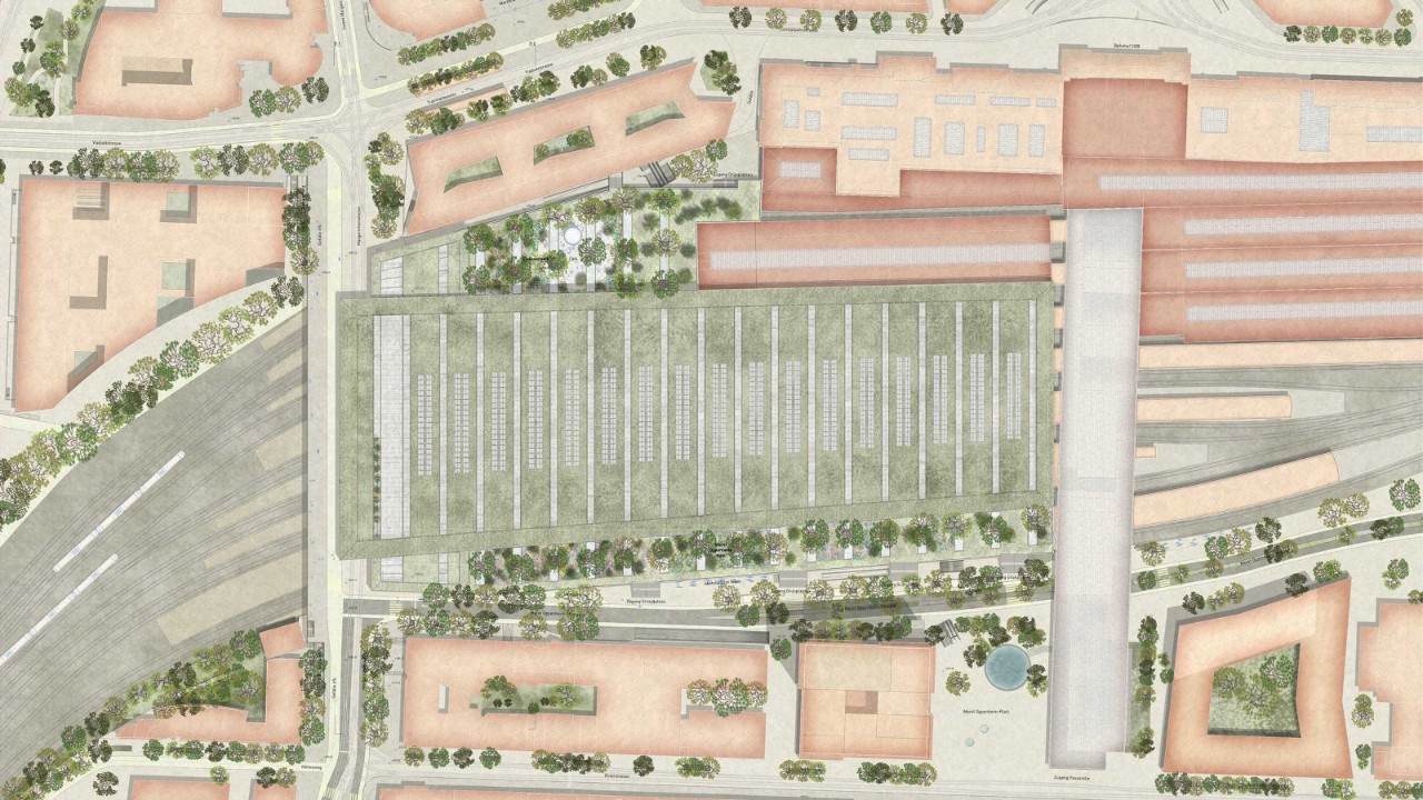 Das Bild zeigt eine detaillierte Luftaufnahme eines Bahnhofsbereichs mit mehreren Gleisen, Perrons und umliegenden Gebäuden. Es gibt Bäume und Grünflächen um den Bahnhof herum. Die Straßen und Wege sind ebenfalls deutlich zu erkennen.