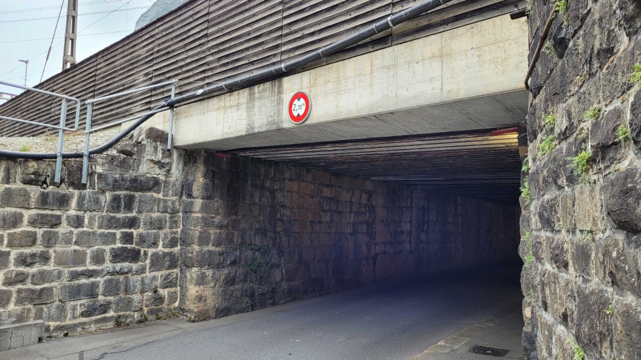 Das Foto zeigt die Unterführung Schlossbergstrasse in Erstfeld in ihrem Zustand vor Start des Bauprojekts in einer Ansicht von der Südseite her. Die Unterführung ist düster, aus dem Mauerwerk wachsen teilweise Pflanzen.