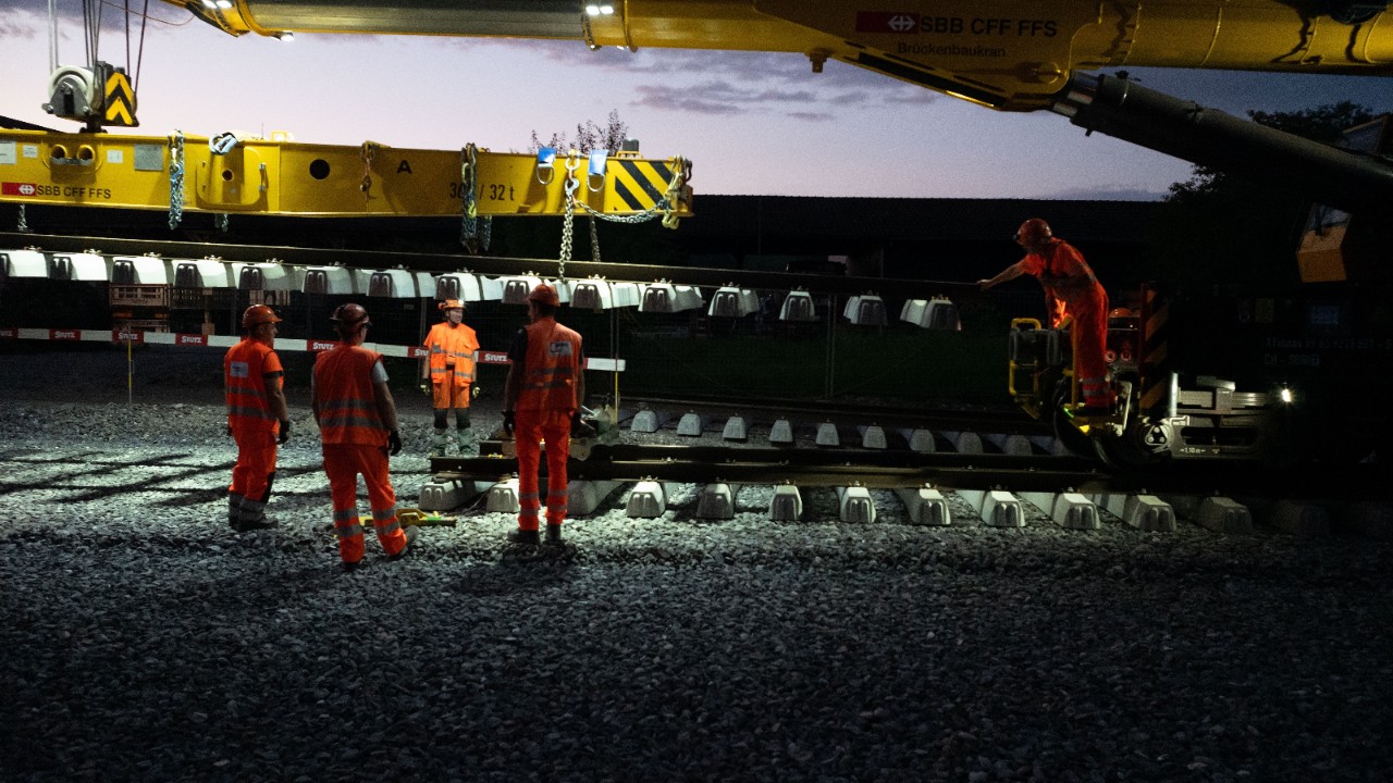 Das Foto zeigt Gleisarbeiten in der Nacht im Bahnhof Pfungen. Mit grossen Baumaschinen werden Gleiselemente auf der vorbereiteten Schotterung platziert.