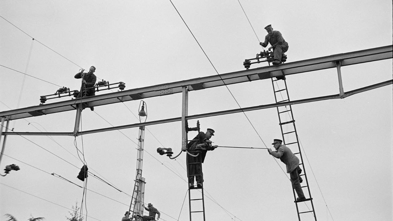 Uniformed SBB workers on ladders working on the overhead line equipment to electrify the rail network.