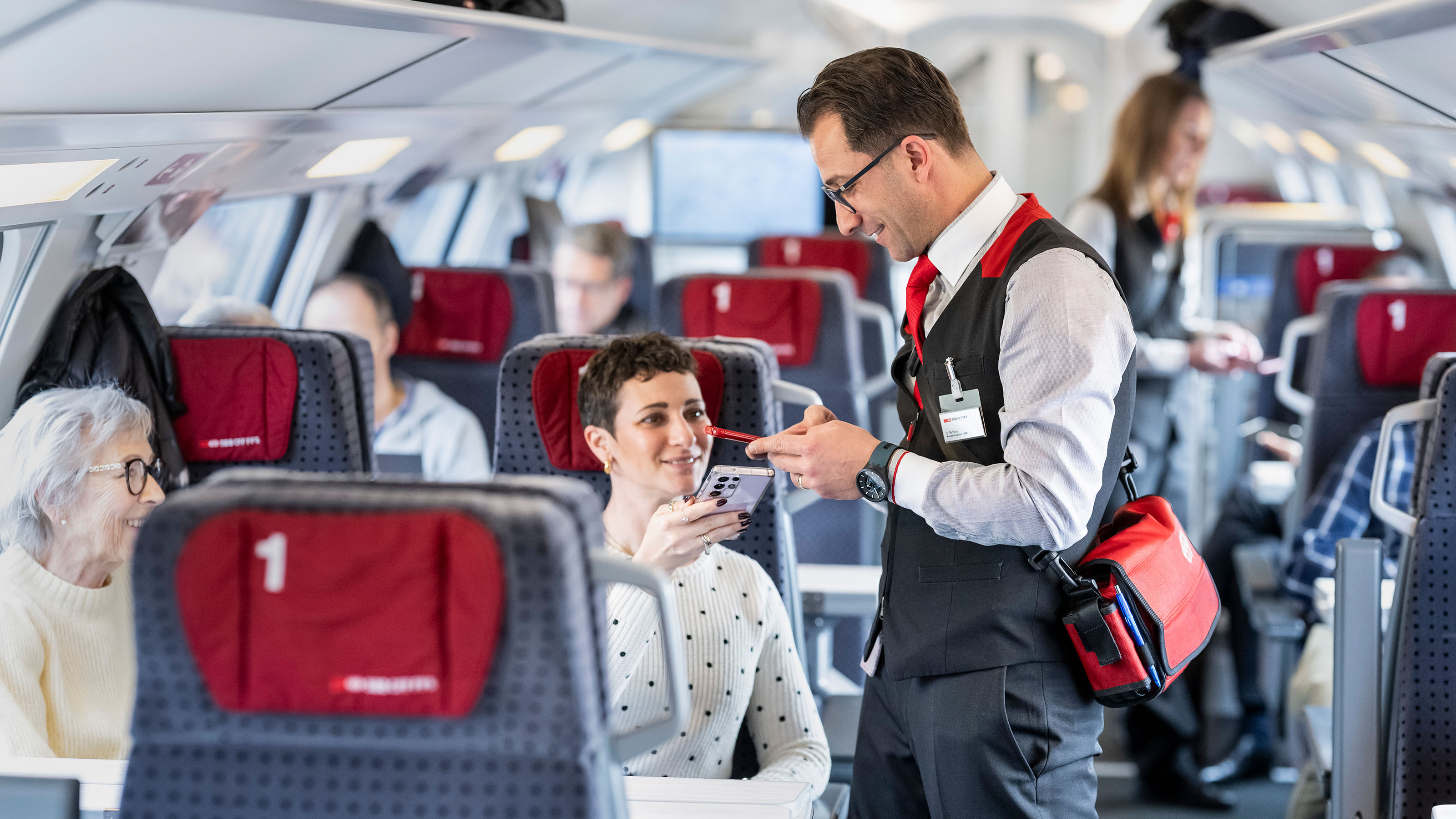 A member of train crew inspects passengers’ tickets in first class, 2025.