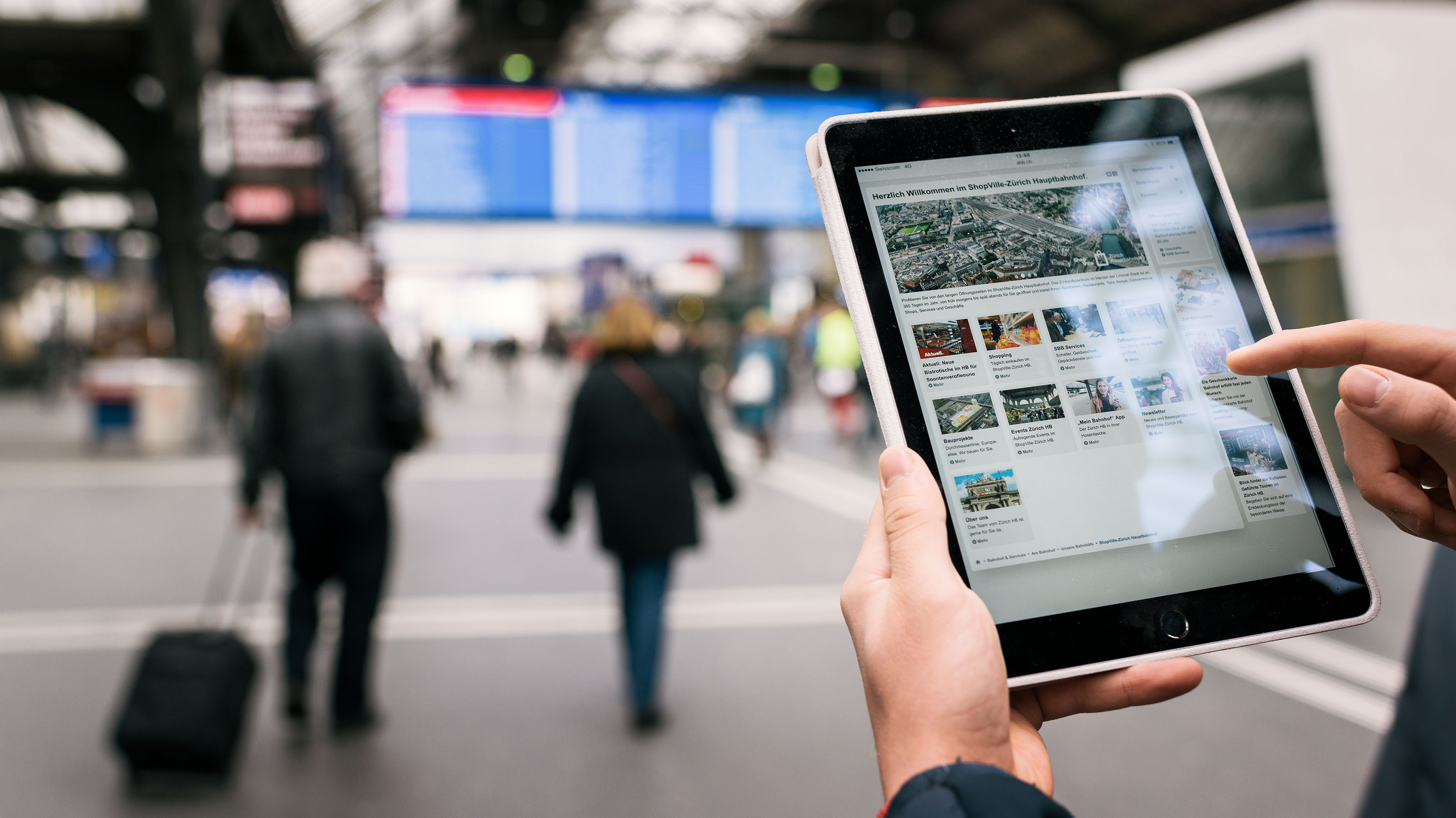 A person standing in a station is holding a tablet and looking for information online, 2017.