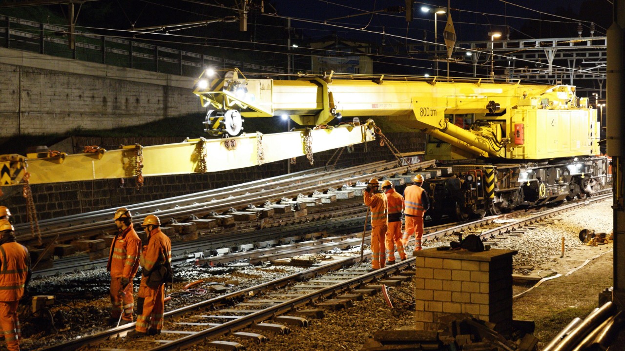 Das Bild zeigt ein Bauarbeitsteam der SBB, das mit grossen Maschinen während einer nächtlichen Gleissperrung Schienen ersetzt.