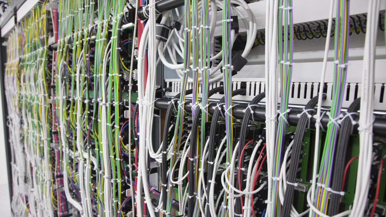 Das Foto zeigt einen offenen Rechnerschrank in einem SBB Stellwerk mit all seinen unzähligen Kabel.