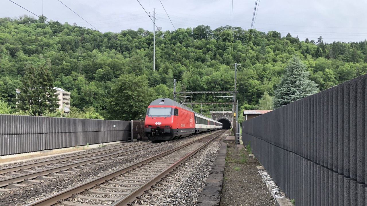 Das Foto zeigt das Südportal des Hauenstein-Basistunnels bei Trimbach im Jahr 2020. Ein einstöckiger Fernverkehrszug gezogen von einer roten IC-2000-Lok verlässt gerade den Tunnel.