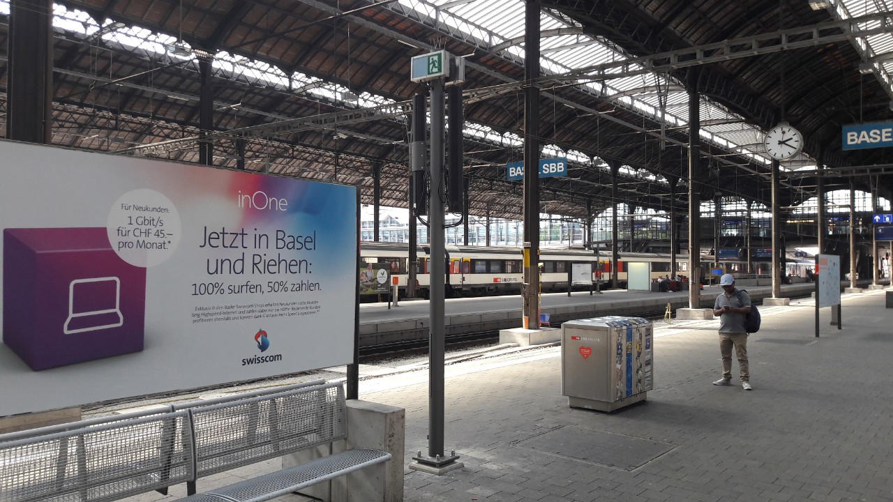 Das Foto zeigt die Musterstele auf dem Perron Gleis 5/6 im Bahnhof Basel SBB. Es ist eine T-Stele mit seitlichen Auslegern. An der schmalen eckigen Säule sind bereits die beiden künftigen, rohrartigen Lautsprecher montiert. 