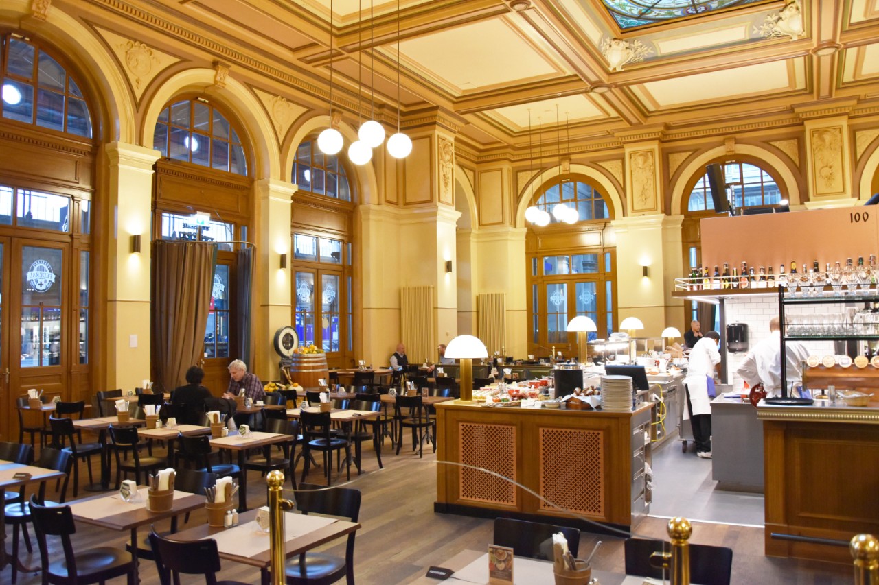 Der historische Speisesaal der Brasserie Federal mit hohen Decken und Aussicht in die Bahnhofshalle.