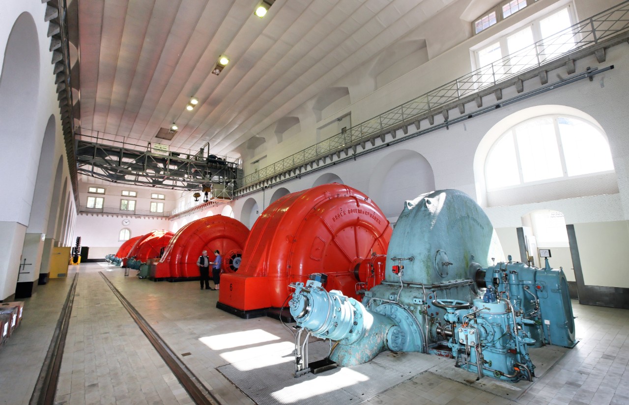 Salle des turbines de la centrale électrique CFF «Centrale Ritom». Deux personnes se parlent à côté d’une turbine. 