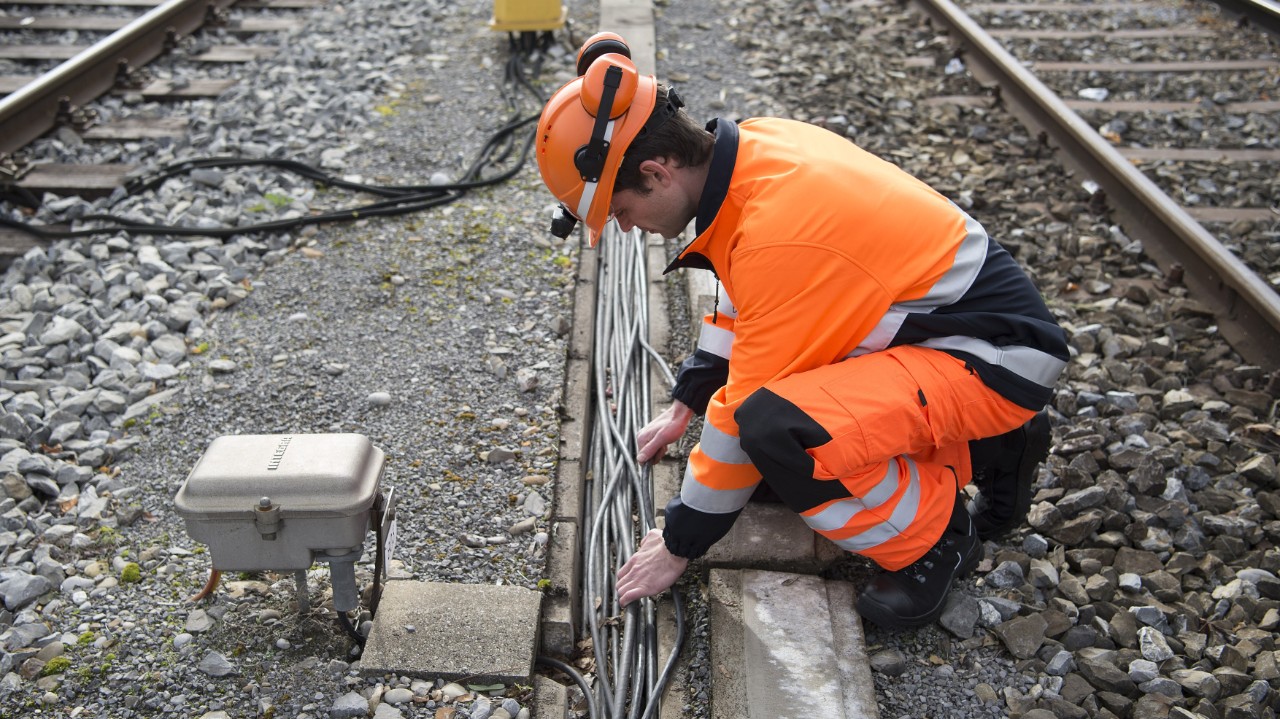 Das Foto zeigt einen SBB-Mitarbeiter, der zwischen zwei Gleisen Arbeiten an einem Kabelkanal vornimmt.