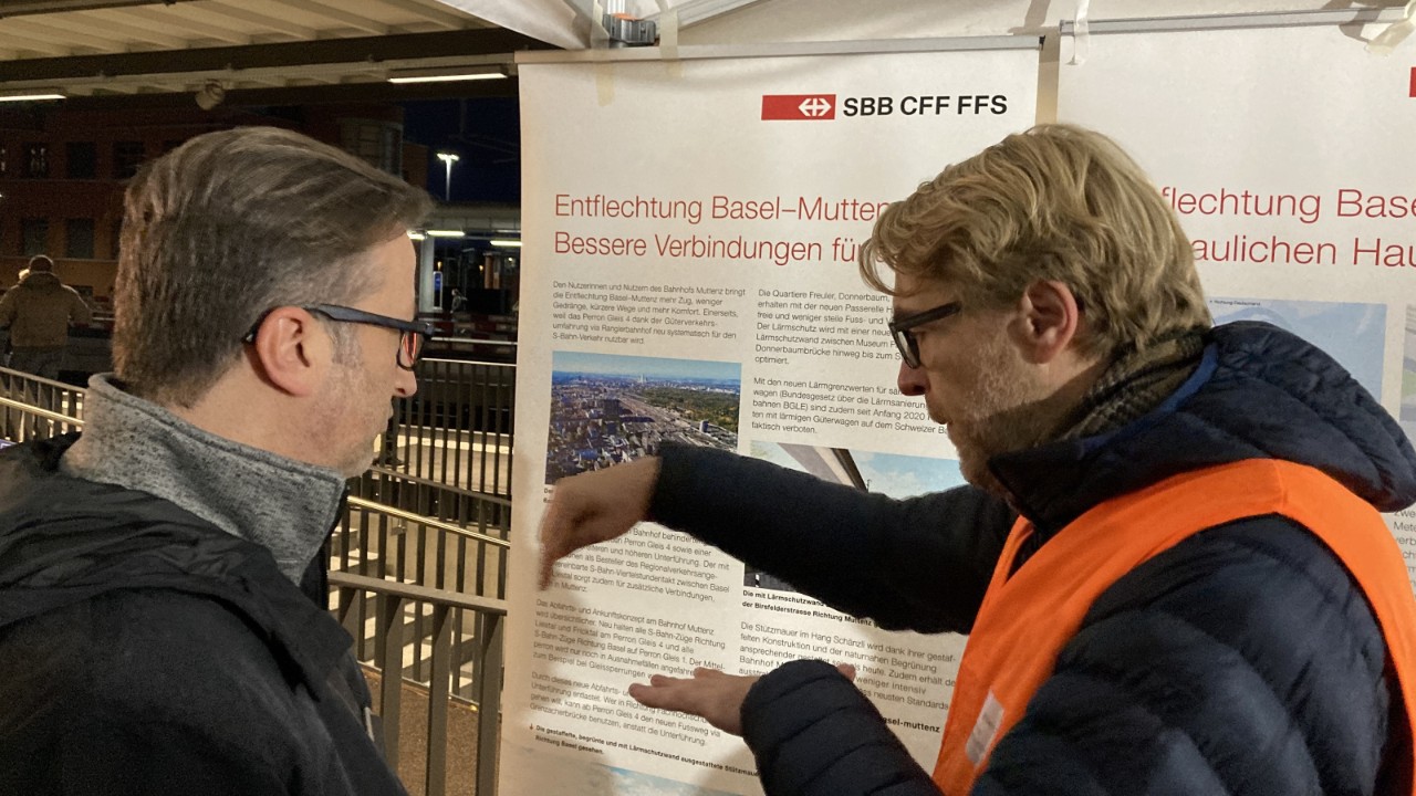 Das Foto zeigt Gesamtprojektleiter Marko Kern, der im Infozelt Redaktor Axel Mannigel mit Gesten die Entflechtung des Bahnsystems bei Muttenz erläutert.