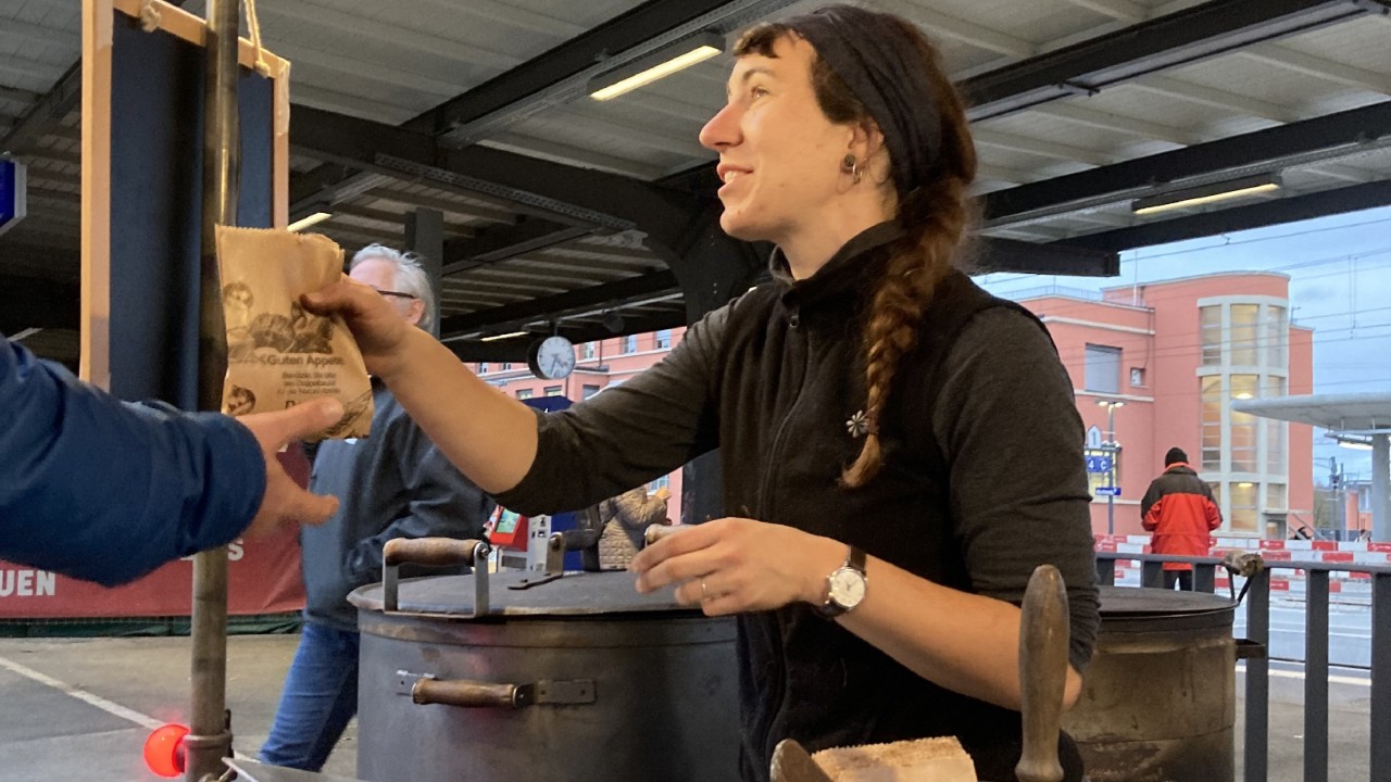 Das Foto zeigt die Marronifrau, die am Bahnhoffest eine Portion Marroni an einen Passanten gibt.