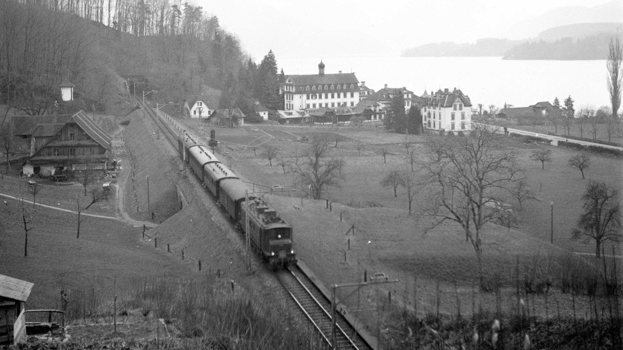 Das Schwarz-Weiss-Bild aus dem Jahr 1946 zeigt einen Zug, der auf der Strecke Meggen–Luzern durch das Gebiet Luzern Seeburg fährt. Die Landschaft ist ländlich mit vielen unbebauten Flächen, im Hintergrund ist der See zu sehen.